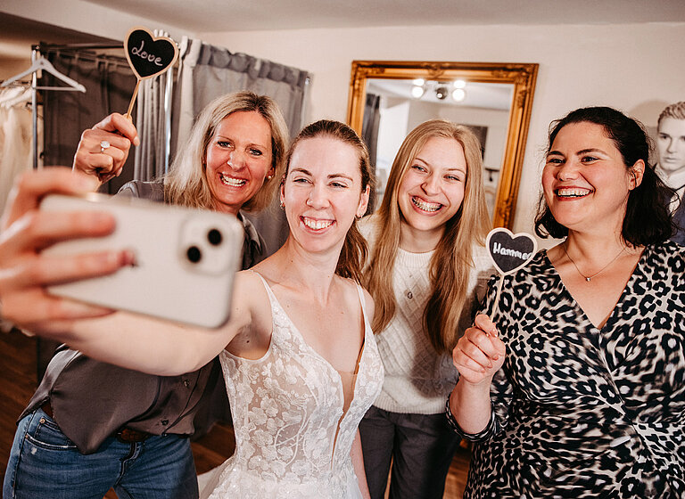 Glückliche Braut macht Erinnerungsselfie mit Freundinnen bei Anprobe
