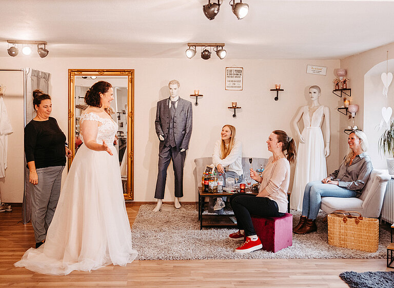 Glückliche Braut zeigt bei Anprobe Kleid ihren Freundinnen