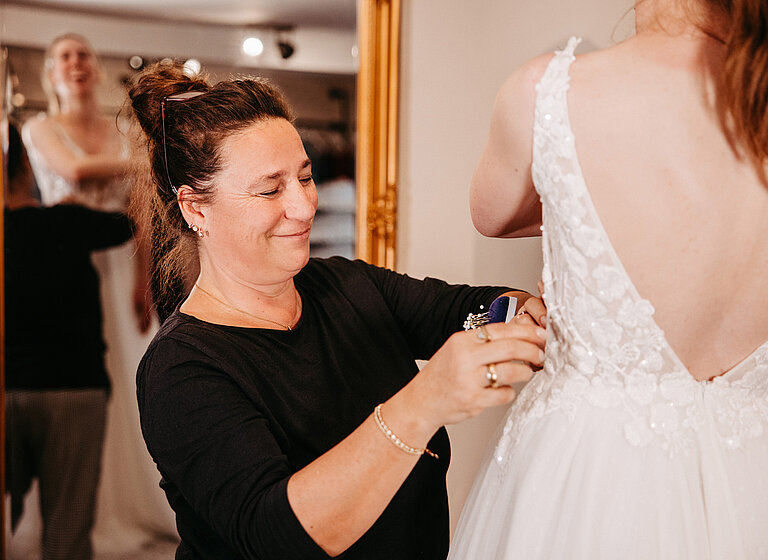 Verkäuferin steckt Brautkleid bei Brautkleidanbrobe ab