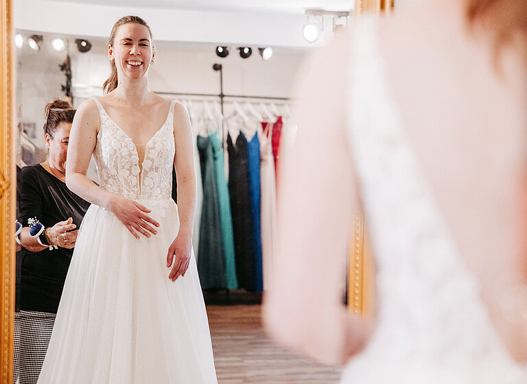 Braut betrachtet sich im Spiegel während der Anprobe des Brautkleids